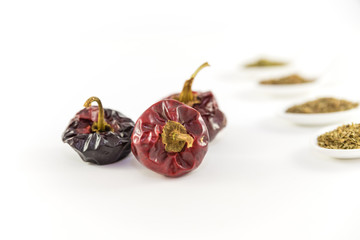 some noras, spanish dry peppers with assorted spices behind on a white background