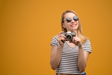 Cheerful hipster girl with retro camera on a yellow background