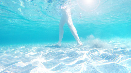 Underwater photography. Legs of a girl in the azure transparent sea. Travel background.