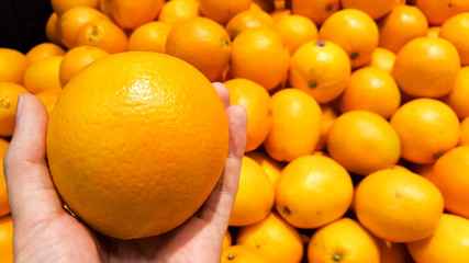 An orange on a hand with group of oranges in supermarket