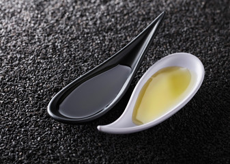 Sesame oil in small bowls on a background of black sesame.