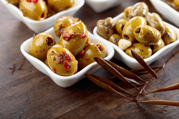 Spiced green olives in oil on a wooden table.