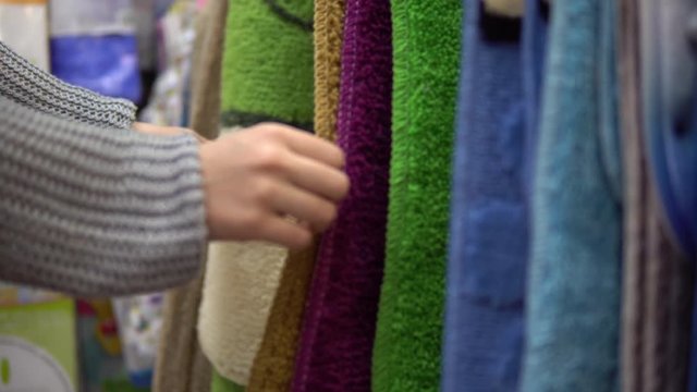 Female hands touch the colored mats to choose a new carpet for the bath or bedroom in the store.