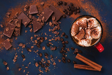 Hot chocolate in a mug with marshmallows and chocolate slices on a blue background. Top view, selective focus. Copy space. Flat lay