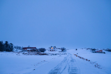 Fototapeta na wymiar Late evening shot of remote farm surrounded with snow in winter, Iceland. Cold winter evening in Icelandic countryside.