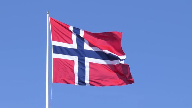 A Norwegian flag fluttering in the wind, set against a clear blue sky.