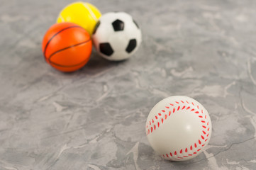 One new rubber soft baseball ball on background of three different sports balls on old worn cement