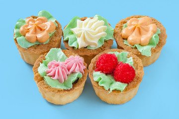 Five cakes with cream on top, in the shape of flowers and berry, on a light turquoise background