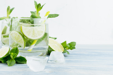 Tropical fresh cold cocktail with mint, lime, ice, straw on light white background, copy space, closeup.