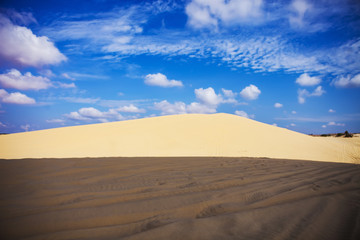 Fototapeta na wymiar Sand dunes near Mui Ne. Group of off roads on top of dunes in the background. Sunny day with blue sky and clouds