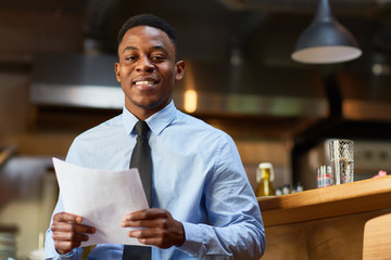 African-american agent with several financial papers looking at camera while waiting for client in cafe