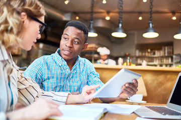 Young businessman with touchpad looking at his colleague explaining online statistics