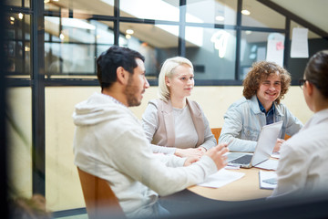 Several young colleagues sitting by table in office and discussing ideas at start-up meeting