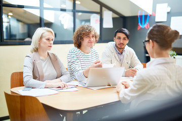 Obraz premium Young businessman and his colleagues listening to creative designer while sitting by table