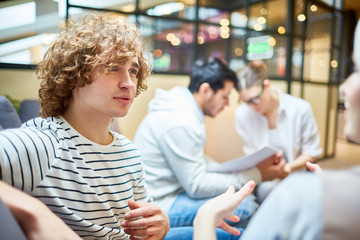 Young curly guy talking to one of colleagues about forthcoming business event in office