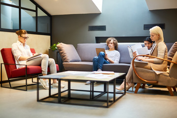 Four young managers sitting in office and preparing for conference: writing down their ideas in notepads, looking for the new ones and making plans of their reports with points