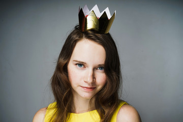 beautiful elegant young woman in a yellow dress looks at the camera, on her head a golden crown
