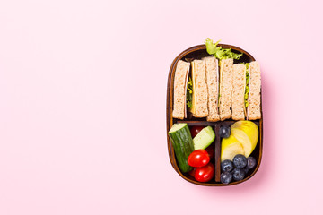 School wooden lunch box with sandwiches, vegetables, , tomatoes and fruits on pink background....