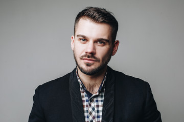 Obraz premium Close up portrait of handsome young business man in shirt and black jacket looking at the camera isolated on grey background in the studio