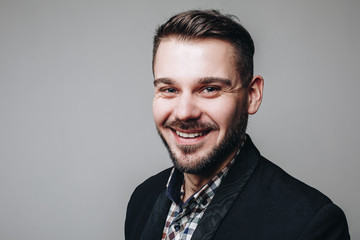 Close up portrait of handsome smiling businessman in casual shirt and black jacket looking at the camera in the studio agains grey background