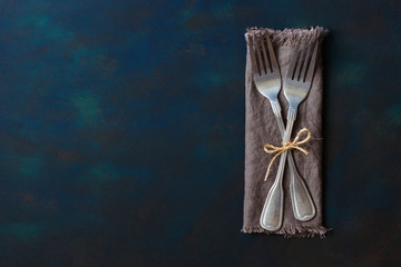 Two vintage forks tied with linen thread on a blue background. Space for text, lay flat