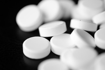 White pharmaceutical pills on a black background close up