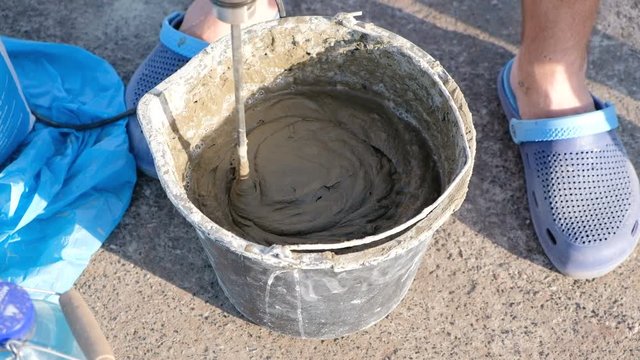 Close up shot of a builder mixing cement in a bucket on a constraction site with a special tools.