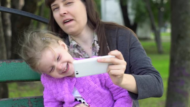 Mom with daughter are doing selfie or make a video call, the family shares their good mood with the person using the smartphone.