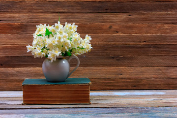 bouquet of Jasmine flowers in a jug on an old book on a table on a brown wooden retro background with copy space