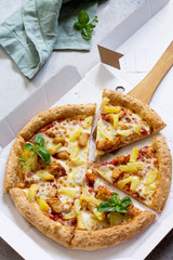 Pizza Hawaiian in a cardboard box on a light stone or concrete background. Pizza delivery.
