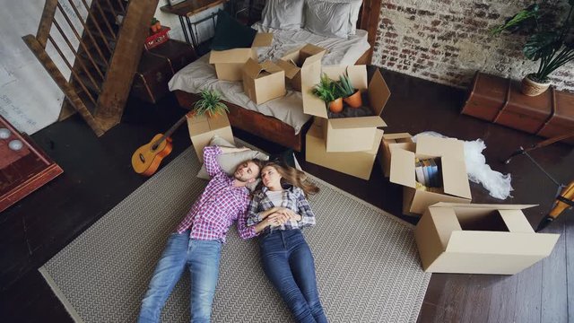 Top view of attractive husband and wife lying on bedroom floor in new house and having conversation. Young family, relationship and relocation concept.