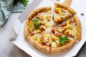 Pizza Hawaiian in a cardboard box on a light stone or concrete background. Pizza delivery.