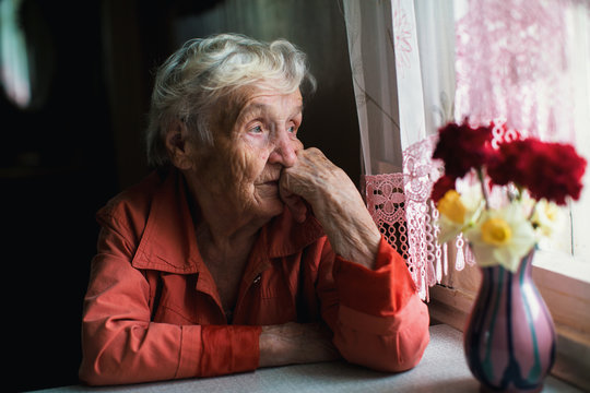 Elderly woman looks sadly out the window.