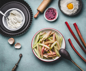 Peeled and sliced rhubarb in bowl on kitchen table background with  with cooking and baking tools, top view. Seasonal food concept.  Rhubarb cake preparation.