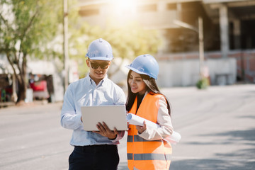 Asian man and woman engineer with the blue safety helmet meeting at the construction site with...