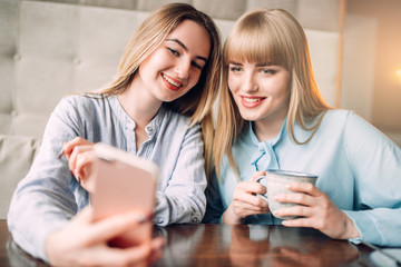 Young woman shows photos to her girlfriend in cafe