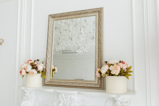 square vintage mirror frame on the livingroom wall over fireplace with photo frame, and flowers bouquet
