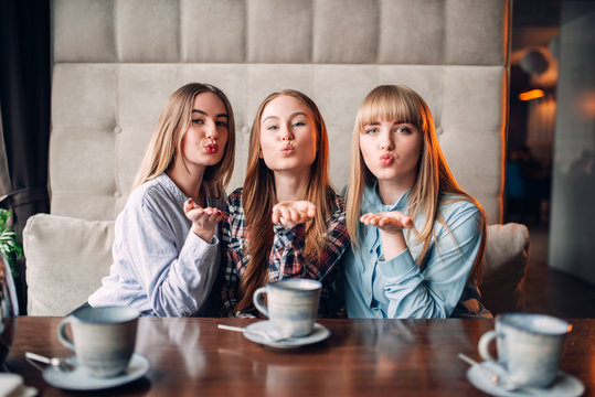 Three attractive girlfriends blow a kiss in cafe
