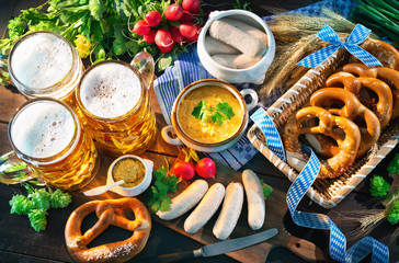 Bavarian sausages with pretzels, sweet mustard and beer mugs on rustic wooden table