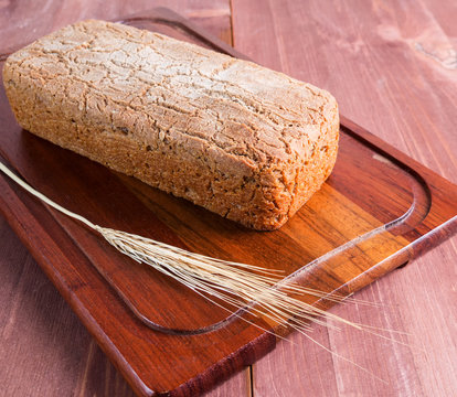 Homemade baked bread and a stalk of wheat on a cutting board