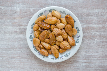 Fried almonds, typical Spanish appetizer, on a round plate on a gray wooden table.