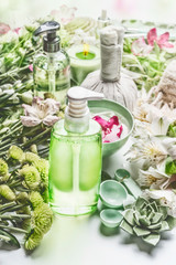 Spa setting with green cosmetic bottle product with pump dispenser , flowers and herbs, beauty tools and accessories for skin and body care