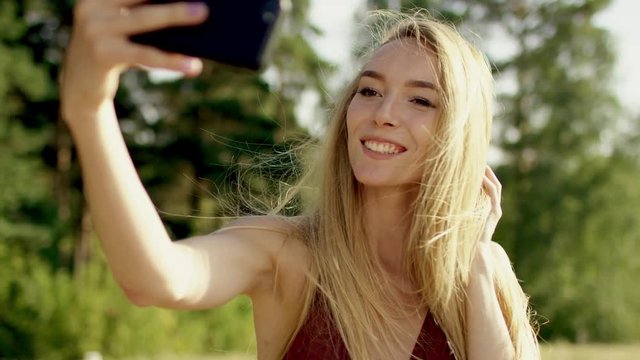 beautiful blonde brown-eyed long-hair girl making selfi with her phone frome up to view in brown swimsuit and bikini a background of nature