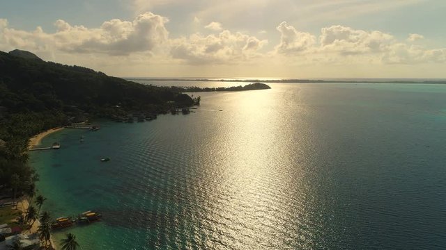 Aerial view of tropical paradise of Bora Bora island, crystal clear water of scenic blue lagoon at sunrise, sun light reflection on water - South Pacific Ocean, French Polynesia from above, 4k UHD