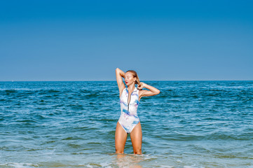 Fototapeta premium Summer. Beautiful tanned woman in swimsuit is coming out of the ocean