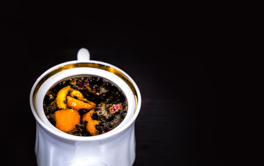 White porcelain brewer or kettle with a golden border without a lid on a dark background. Brewed tea with orange and flowers