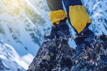 Climber in crampons stands on the rocks in front of the entrance to the peak on the background of the snowy mountains.