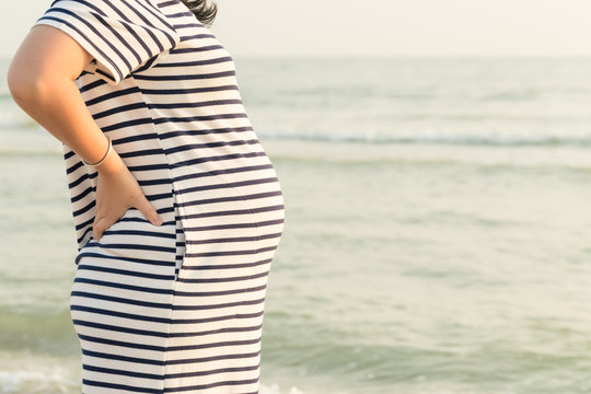 Pregnant woman holding her belly on the beach with copy space in the morning time.