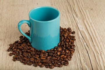Grains of coffee on a wooden background in large quantities and a cup