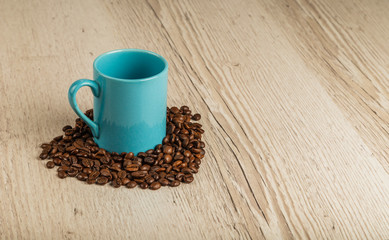 Grains of coffee on a wooden background in large quantities and a cup